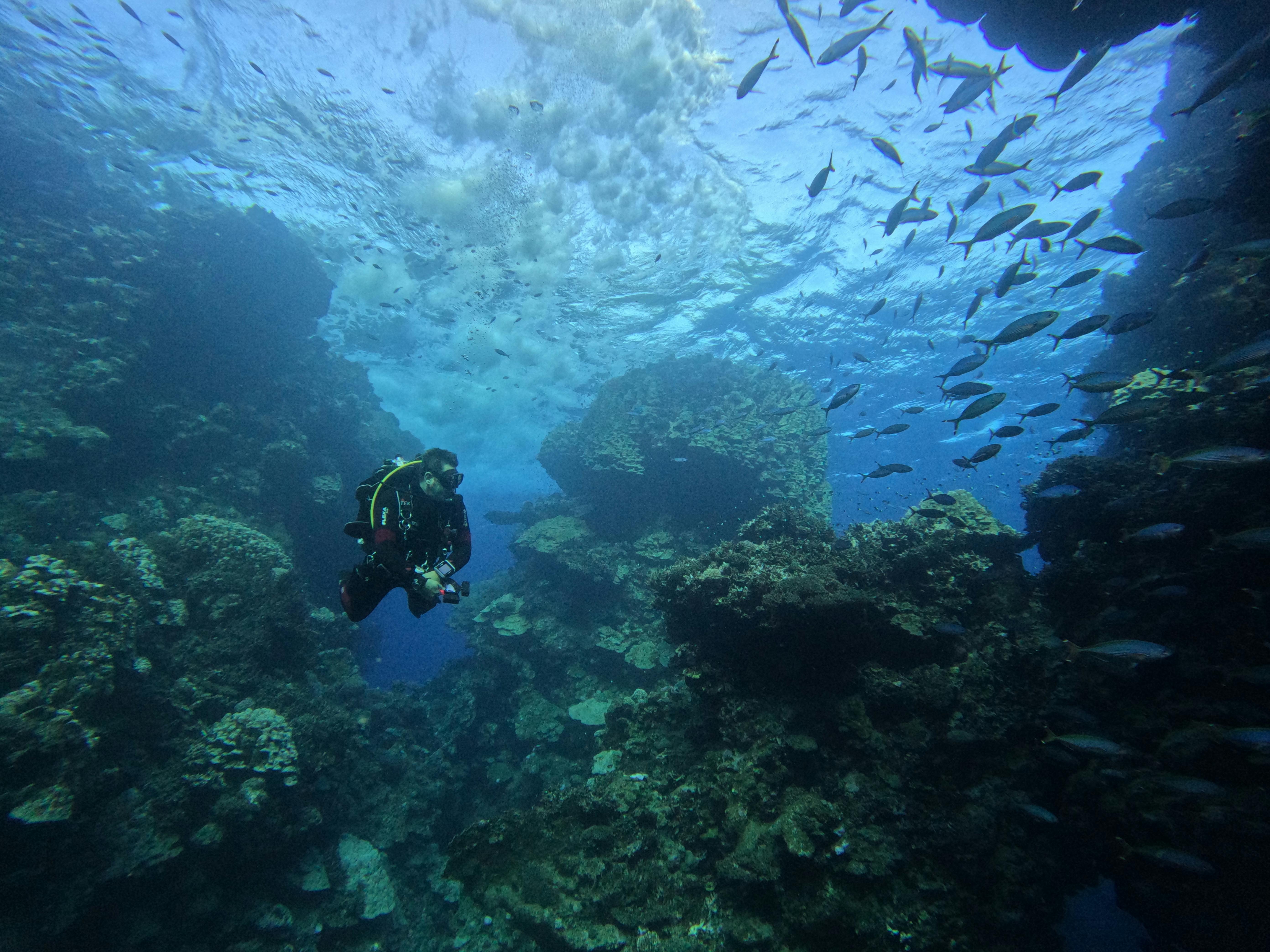 Diver's silhouette against a deep blue cavern opening, vertical descent feel.